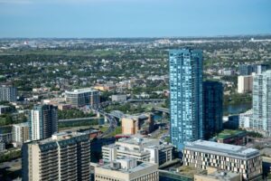 Aerial view of a city skyline with a tall blue glass skyscraper beside a river and a curving highway nearby.